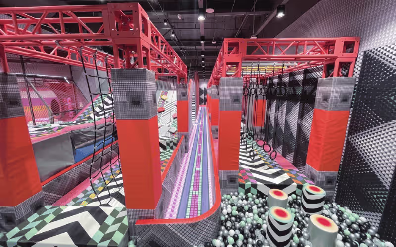 Indoor kids obstacle course playground with orange geometric structure, climbing ropes, balance track and ball pit Indoor kids obstacle course playground with orange geometric structure, climbing ropes, balance track and ball pit